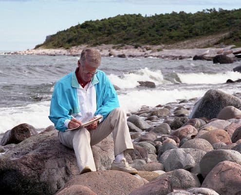 Ingvar Carlsson sitter och skriver på en stenstrand